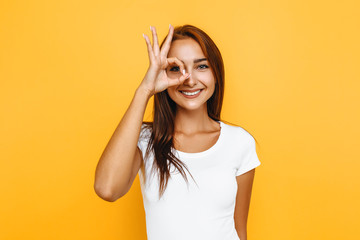 Young cheerful girl showing zero gesture on a yellow background - obrazy, fototapety, plakaty