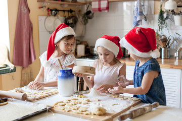 Kids cooking Christmas cookies in cozy kitchen. Cute sisters prepare holiday food for family together. Cute girls bake homemade festive biscuits. Lifestyle moment. Santa helpers. Children chef concept