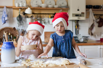 Children are cooking Christmas cookies in cozy home kitchen. Cute kids prepare holiday food for family. Funny little sisters in flour make New Year meal. Lifestyle candid moment. Children chef concept