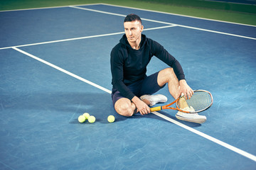 portrait of a male tennis player. young guy with a racket in his hands sitting on the court.