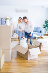 Young beautiful couple with dog hugging at new home around cardboard boxes