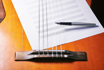 on the guitar are a white sheet with notes and a pen.