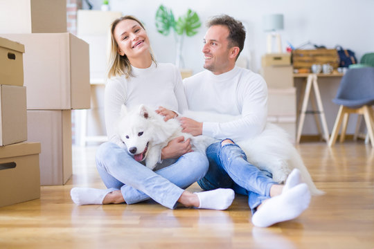 Young beautiful couple with dog sitting on the floor at new home around cardboard boxes