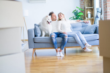 Obraz premium Young beautiful couple with dog sitting on the sofa at new home around cardboard boxes