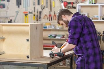 Young bearded man working at the furniture factory