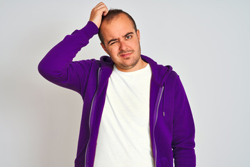 Young man wearing purple sweatshirt standing over isolated white background confuse and wonder about question. Uncertain with doubt, thinking with hand on head. Pensive concept.