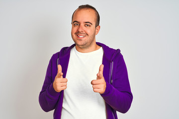 Young man wearing purple sweatshirt standing over isolated white background pointing fingers to camera with happy and funny face. Good energy and vibes.