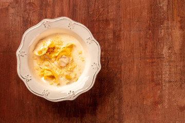 Italian tortellini in a cream sauce with grated Parmesan cheese, shot from above on a dark rustic wooden background with copyspace