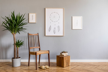 Stylish bohemian interior design of living room with retro chair, wooden cube, flowers , tropical plant, mock up poster frames and elegant accessories. Modern home decor. Template. Gray background.