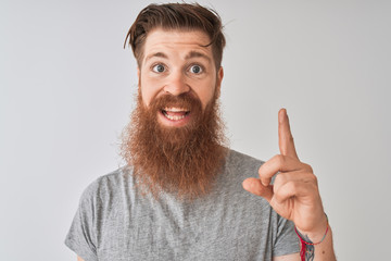 Young redhead irish man wearing t-shirt standing over isolated grey background surprised with an idea or question pointing finger with happy face, number one