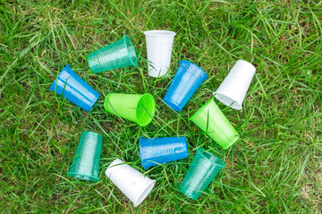 Bright colourful disposable plastic cups isolated on green grass. Ecology problem. 