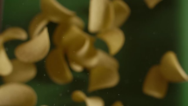 Falling crispy golden potato chips in slow motion on the green background, slow motion food, snacks and fast food, 240p Full HD 10 bit