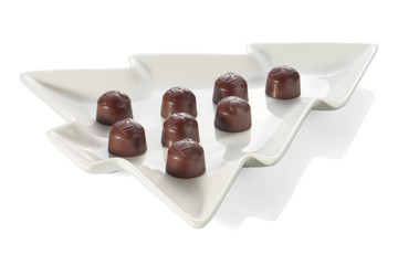 Chocolate candies with cherry filling without wrapper are laid out on a white plate in the shape of a Christmas tree close-up, isolated on a white background with shadows.