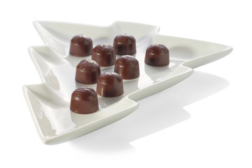 Chocolate candies with cherry filling without wrapper are laid out on a plate in the shape of a Christmas tree close-up, isolated on a white background with shadows.