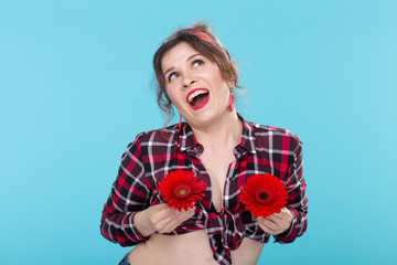Portrait of positive young woman in plaid shirt holding two red flowers with different hearts near...