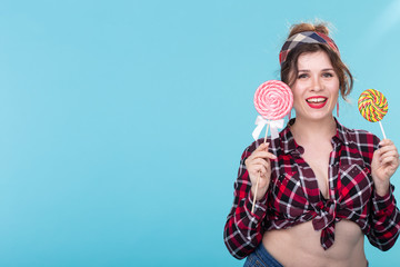 Cheerful laughing pretty young woman in retro clothes posing on a blue background with a lollipops....