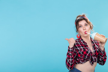Cute charming young woman in retro clothes is drinking a cocktail from a straw posing against a...