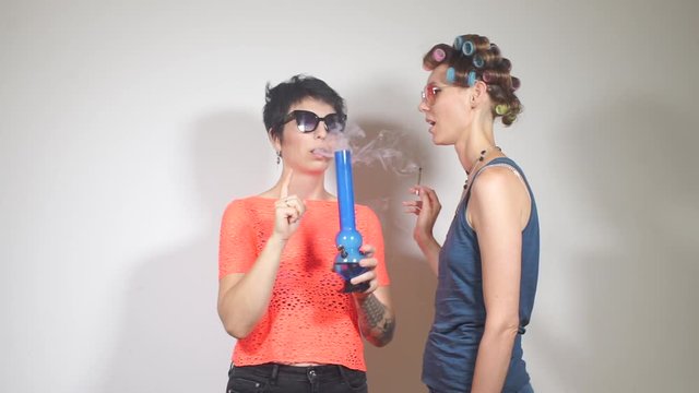 girl with a girlfriend smokes cannabis, exhales smoke from a bong