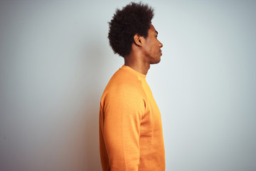 Fototapeta na wymiar Young american man with afro hair wearing orange sweater over isolated white background looking to side, relax profile pose with natural face with confident smile.