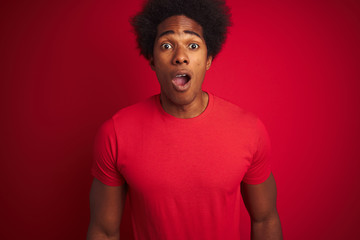 Fototapeta na wymiar Young american man with afro hair wearing t-shirt standing over isolated red background afraid and shocked with surprise expression, fear and excited face.