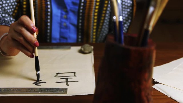 Girl writes Chinese characters (Translation from Chinese Mandarin 1: jixiang ruyi wanshi ankang- to be gratified propitiously with everything in good health, 2: fugui jixiang: wealthy and propitious)