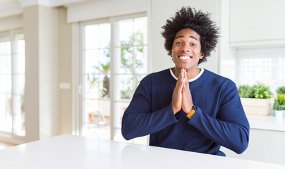 Fototapeta na wymiar Young african american man wearing casual sweater sitting at home praying with hands together asking for forgiveness smiling confident.