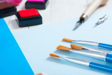 stamp ink pad, lino cutter , papers and rubbers on white wood table