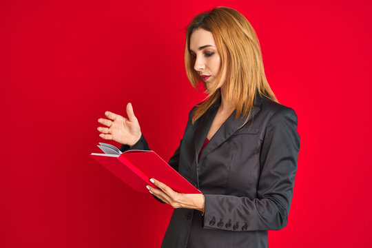 Young beautiful redhead businesswoman wearing suit reading book