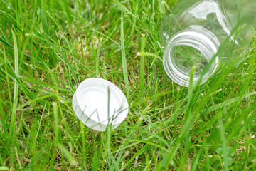 Empty plastic bottle and cap on green grass. Ecology problem. Environmental pollution.