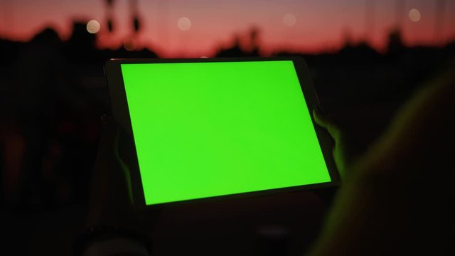 Close up young hands woman uses tablet computer with a horizontal green screen on night street amazing sunset internet map hold pc scroll smart phone social network tourist tracking blank chroma city