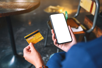 Mockup image of a hands holding credit card and a black mobile phone with blank desktop screen