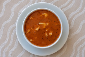 Red tomato soup with dumplings in a white bowl, close up