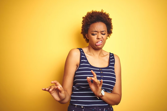 Beauitul african american woman wearing summer t-shirt over isolated yellow background disgusted expression, displeased and fearful doing disgust face because aversion reaction. With hands raised
