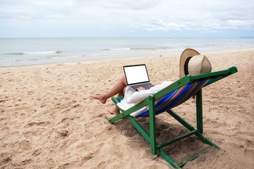 Fototapeta na wymiar Mockup image of a woman using and typing on laptop computer with blank desktop screen while lying down on a beach chair