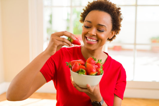 Beautiful young african woman with afro hair eating fresh strawberries