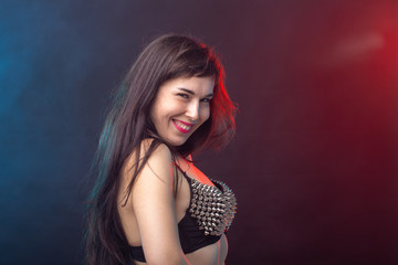 Beautiful young sexy brunette woman posing on a dark background in a riveted top on a dark background. The concept of grooming and attractiveness.