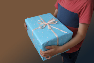 the boy is holding a gift in a big blue box in white peas with a ribbon, copy space