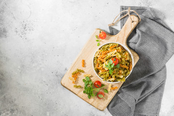 Raw multicolored fusilli pasta in a gray bowl on a light table. Italian cuisine