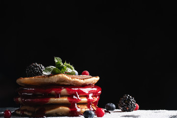Pancake tower with fresh blueberry, chocolate, powdered sugar and mint on a black stone background