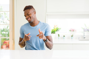Handsome african american man wearing casual t-shirt at home pointing fingers to camera with happy and funny face. Good energy and vibes.