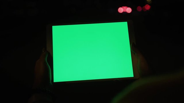Close up young hands woman uses tablet computer with a horizontal green screen on night street internet map hold pc scroll smart phone social network tourist tracking blank chroma city slow motion