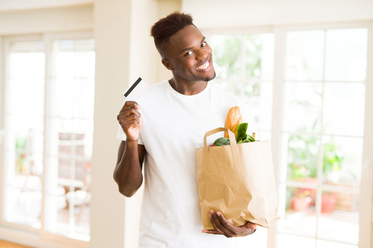 African american man holding paper bag full of groceries and holding credit card as payment