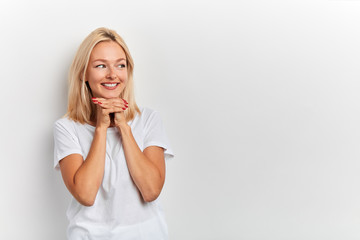 Close up photo of delighted charming girl with palms under chin looking with flirt aside wearing casual whiet T-shirt clothes isolated on white background. copy space. place for text, advert