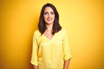 Beautiful elegant woman standing over yellow isolated background with a happy and cool smile on face. Lucky person.