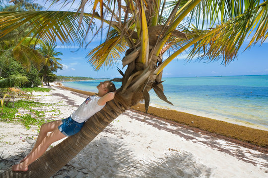 Caucasian teenage girl resting on a palm tree on tropical beach in Sargasso sea, Punta Cana, Dominican Republic. Summer vacation concept