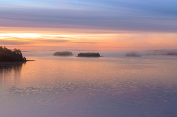 Naklejka premium Long Exposure of Sunset at the Paijanne lake. Beautiful scape with sunrise sky, pine forest and water. Lake Paijanne, Finland.