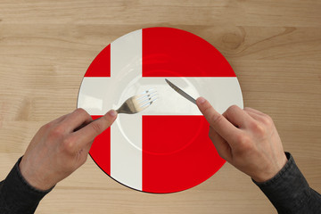 hands with cutlery on a plate with the state national flag of Denmark, copy space