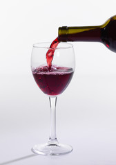 Red wine pouring from bottle into big glass on white