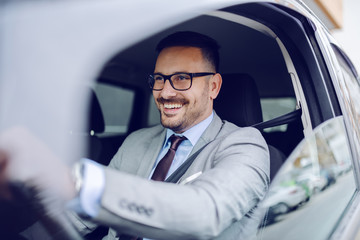 Cheerful caucasian businessman driving himself to work. Hands are on steering wheel.