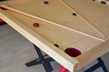 Novuss game wooden board with discs or dices and two pool cues closeup. Sportg similar to pocket billiards.